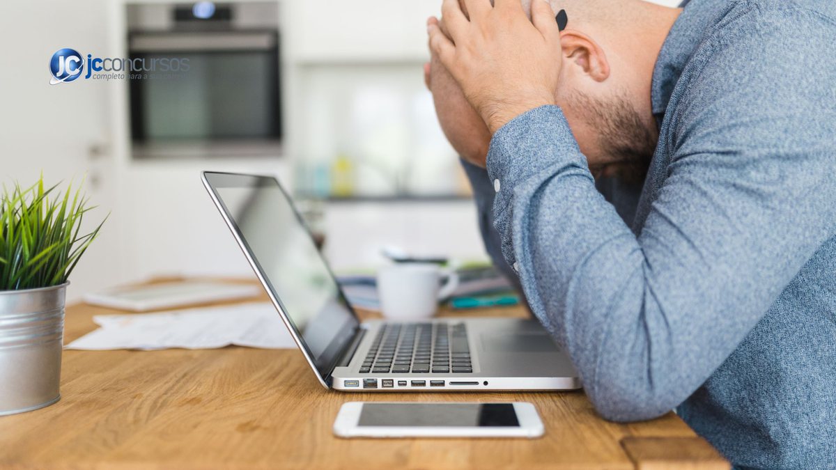 Um homem baixa a cabeça de frente a um notebook - Canva - ansiedade no trabalho