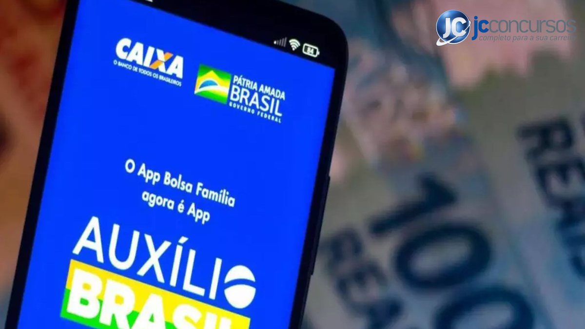 Um celular aberto com o programa do Auxílio Brasil e no fundo notas de dinheiro