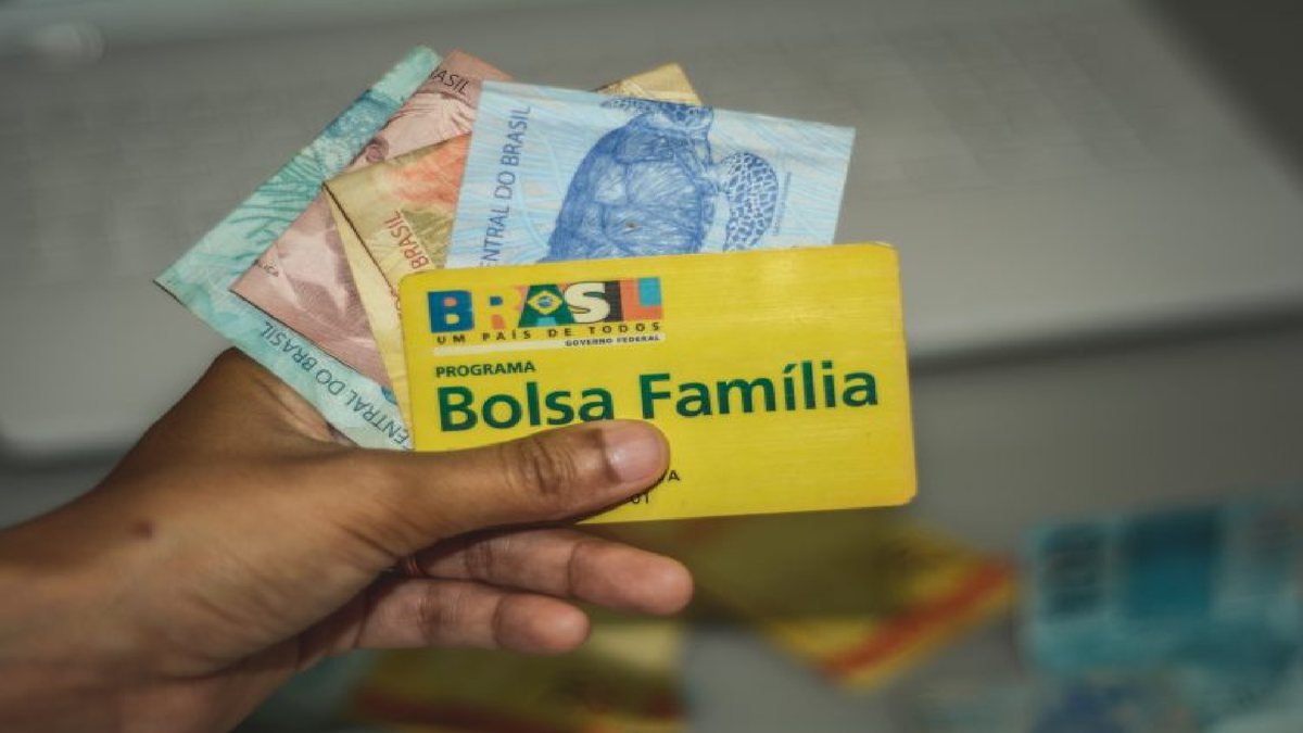 Pessoa segura cartão do Bolsa Família e notas de reais - Divulgação