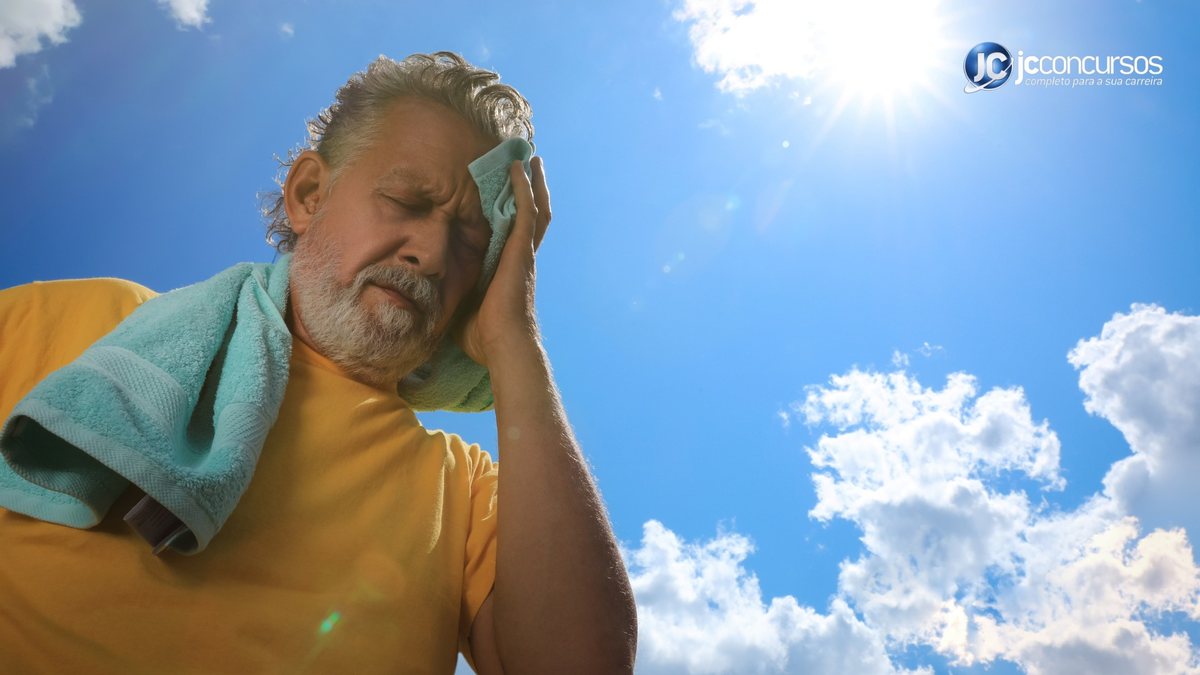Homem seca suor com toalha em dia com céu azul e sol forte