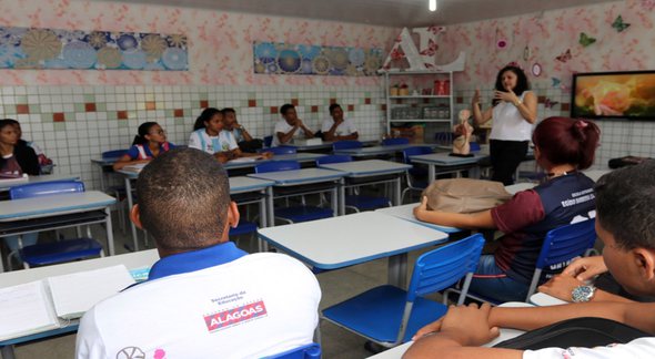 Concurso Seduc AL: sentados em sala de aula, estudantes observam explicação de professora - Divulgação