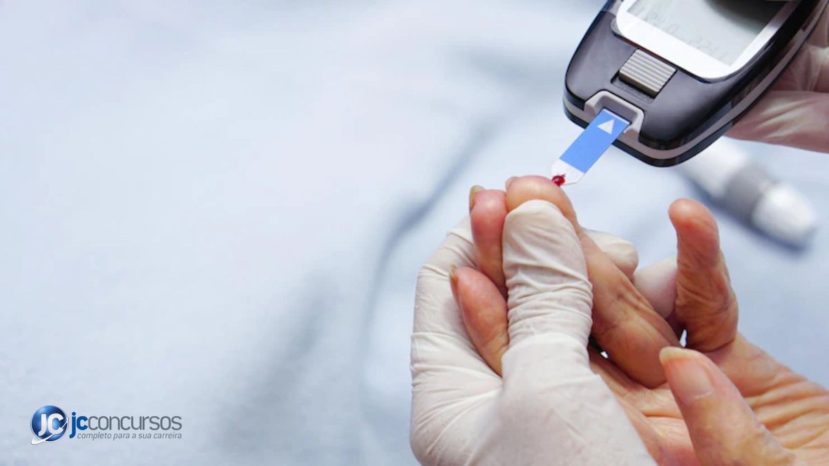 Profissional de saúde colhendo sangue com medidor glicêmico no dedo da paciente
