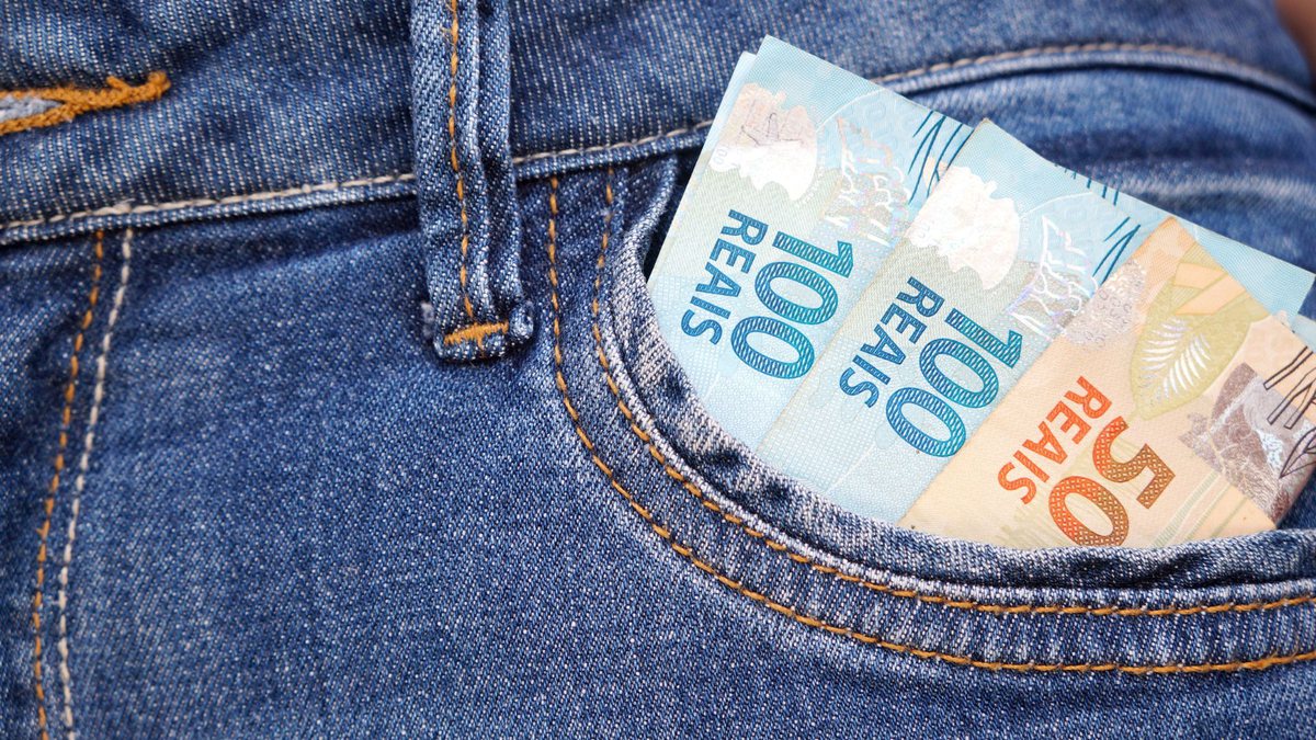 Pessoa com notas de cem e cinquenta reais em bolso de calça jeans