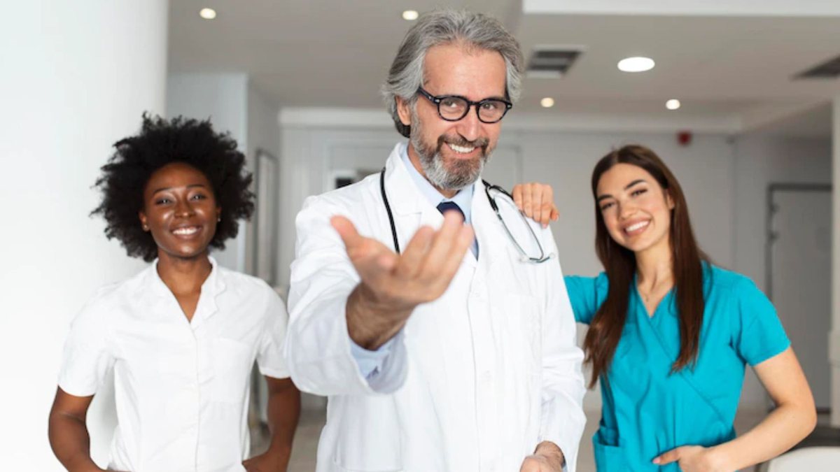 À esquerda: mulher negra, profissional de saúde. Ao centro: homem branco, grisalho, de jaleco e estetoscópio. À sua direita, uma mulher jovem de uniforme de hospital, azul. | Foto: Freepik - None
