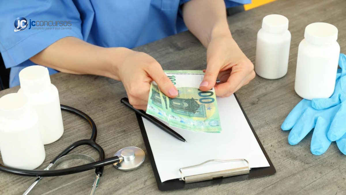 Profissional de saúde contando dinheiro em meio a objetos de trabalho | Foto: Freepik