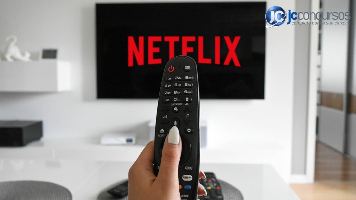 Mão segura controle remoto da TV, que mostra o nome Netflix na tela - Divulgação
