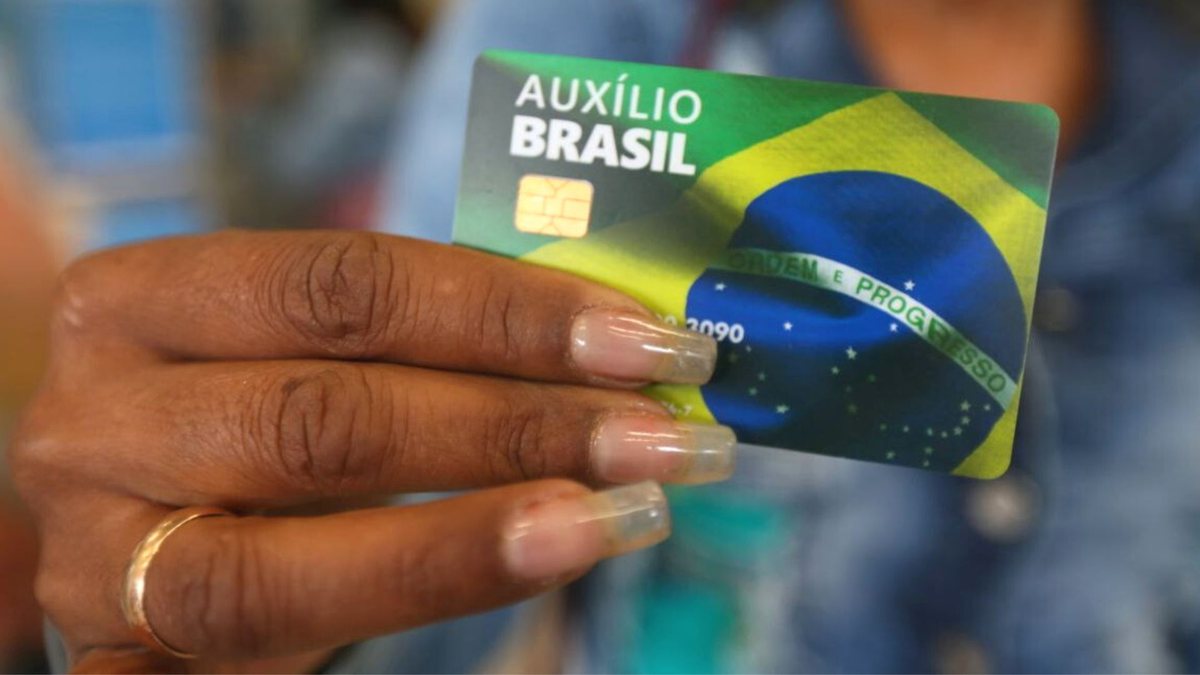 Mulher segura o novo cartão do Auxílio Brasil, com chip