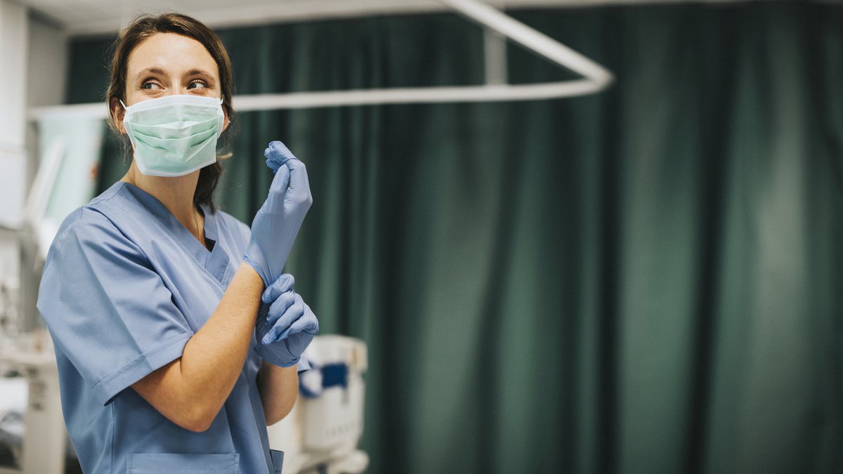 Uma enfermeira ajeita a luva dentro de um hospital