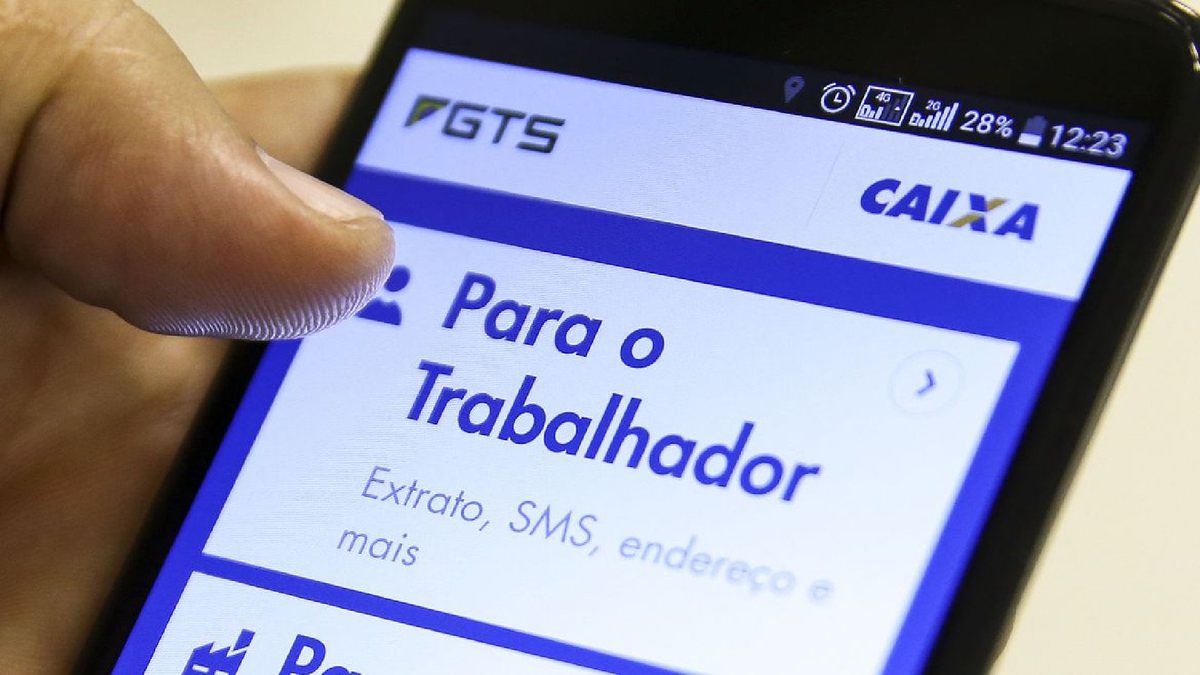 Um homem segura um celular aberto com o site do FGTS - Agência Brasil - PIS/Pasep 2023