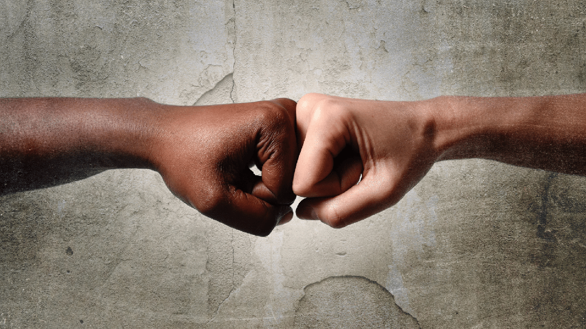 Pessoas branca e negra tocam as mãos com punho fechado - Divulgação