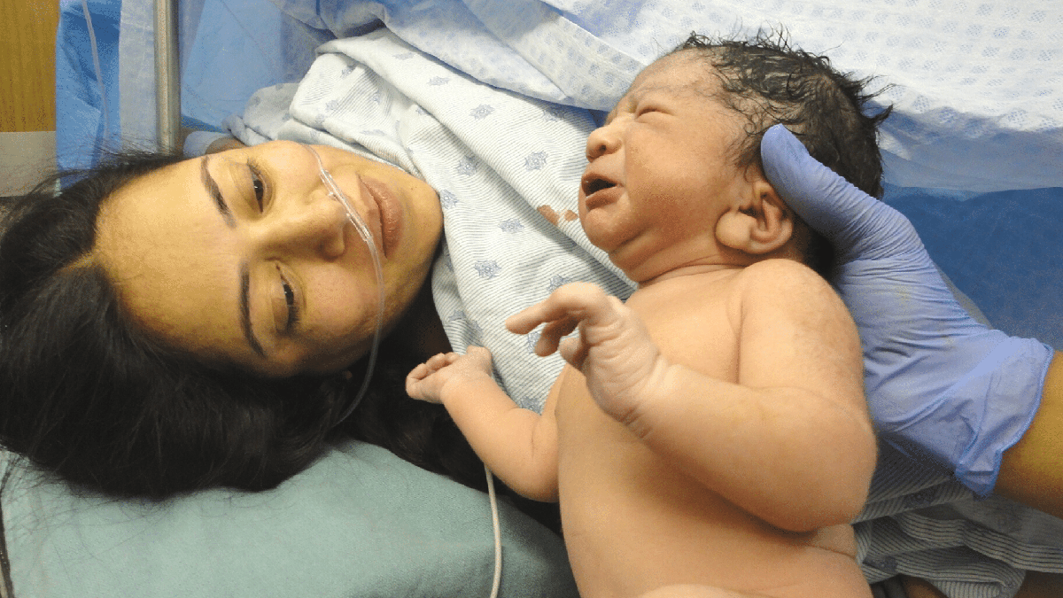 Mãe na cama de parto olha bebê recém-nascido - Divulgação