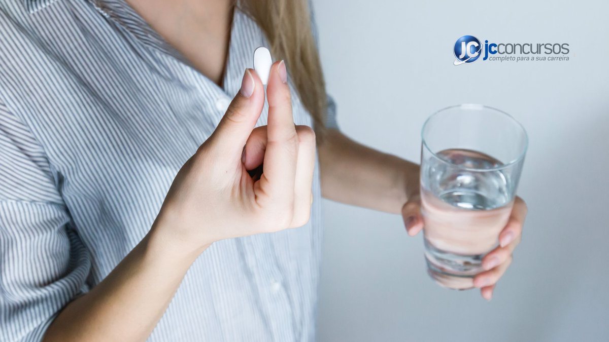 Uma mulher segura um medicamento e um copo com água