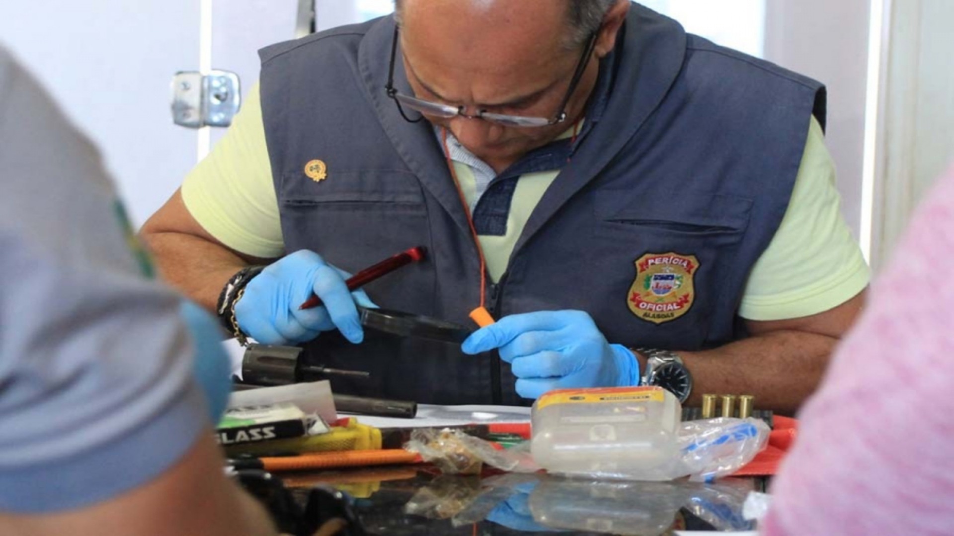 Perito utiliza lupa para examinar arma de fogo